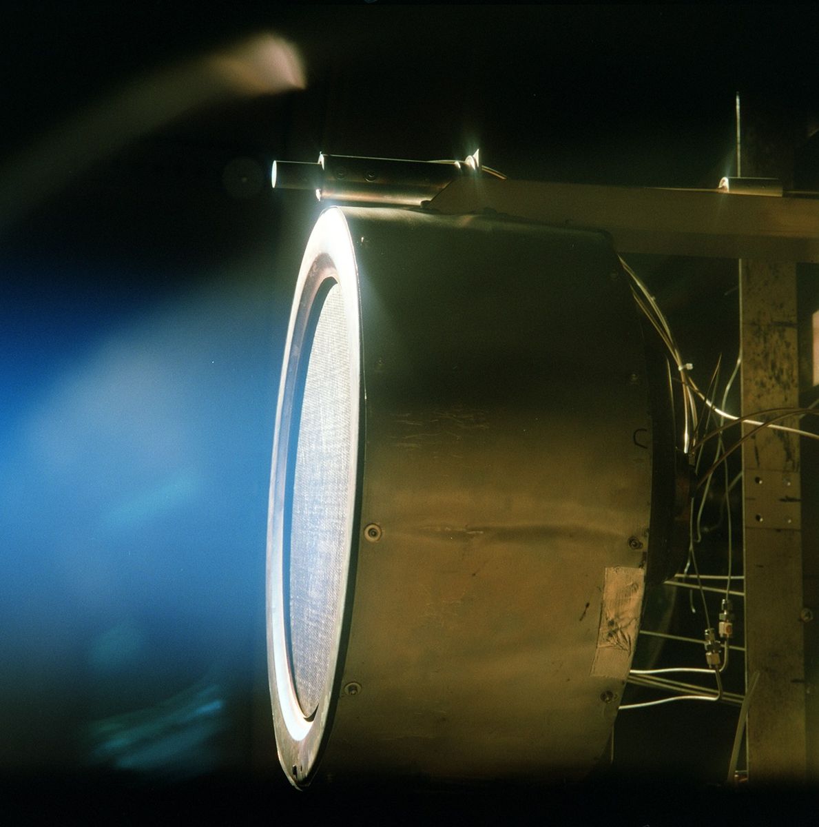 A xenon ion-engine prototype glowing blue inside a laboratory vacuum chamber.