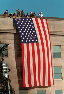 Firefighters unfurl an American flag over the damaged Pentagon on September 12, 2001
